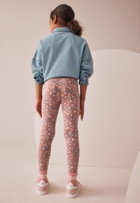 Denimjakke med ballonsærmer, blomsterprintede leggings i bløde pastelfarver og lyserøde sokker kombineret med hvide sneakers.