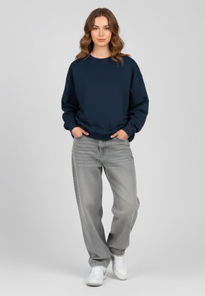 Felpa navy con scollo a girocollo, abbinata a jeans grigi chiari e sneakers bianche. Il tessuto appare morbido, con una vestibilità comoda.