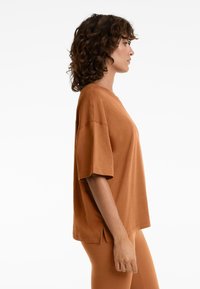 Barna, oversized póló rövid ujjakkal, puha tapintású, kerek nyakkivágással, oldalsó hasítékokkal, azonos színű leggingsszel viselve.