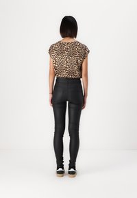 Majica s uzorkom leoparda i rukavima na kapu; crne uske hlače s detaljima šivanja; model nosi crno-bijele tenisice na bijeloj pozadini.