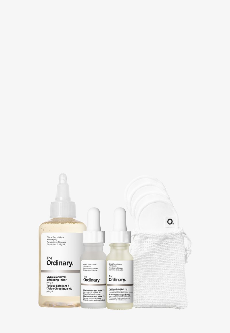 Trois sérums pour la peau avec des compte-gouttes dans des flacons en verre, un marron et deux transparents, accompagnés de coussinets en coton réutilisables dans un sac en mesh blanc.