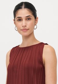 Blouse plissée bordeaux avec un col rond, design sans manches, tissu texturé et un léger fronce aux épaules.
