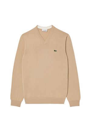 Beige V-hals sweater van zacht materiaal, met geribbelde mouwen en boord, en een klein groen geborduurd krokodillenlogo op de borst.