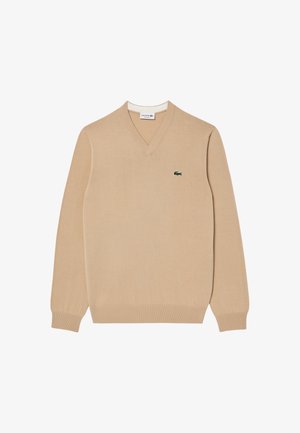 Beige V-hals sweater van zacht materiaal, met geribbelde mouwen en boord, en een klein groen geborduurd krokodillenlogo op de borst.