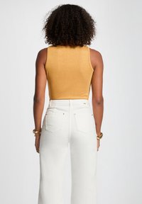 Gold, sleeveless top with a textured finish; paired with high-waisted white jeans featuring two back pockets and metallic accents.