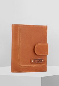 Tan leather wallet with a flap closure, visible stitching, and a branded tag. Features a smooth texture and rectangular shape.