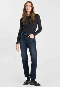 Jeans en denim bleu foncé avec une coupe droite, associés à un haut noir à manches longues ajusté. La tenue présente des détails minimalistes et des chaussures contrastantes.