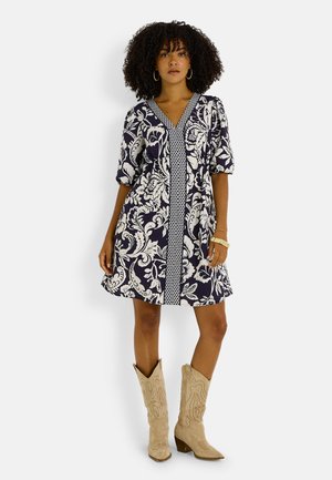 Vestido azul marino con flores, escote en V, mangas abullonadas y un panel central estampado; combinado con botines estilo vaquero beige.