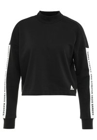 Sweat-shirt noir court avec un col haut, des manches longues, du texte blanc et des rayures sur les manches, fabriqué en tissu doux, arborant un logo Adidas.