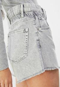 Pantalones cortos de mezclilla gris con dobladillo deshilachado, cinturilla elástica y dos bolsillos traseros. La tela parece ligeramente desgastada.