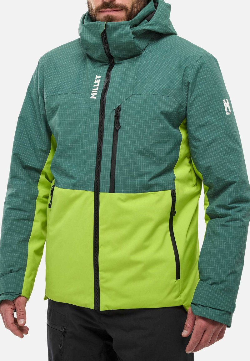 Veste isolante bicolore vert et lime avec un motif en grille, fermeture éclair intégrale, capuche réglable et accessoires noirs. Comprend des poches latérales zippées.