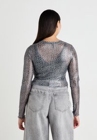 Sheer long-sleeve top with gray and black leopard print, featuring a round neckline and fitted silhouette, paired with high-waisted gray jeans.