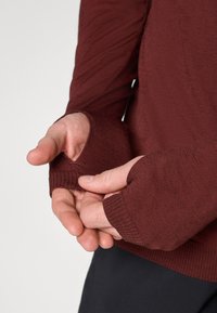 Bordo dugih rukava s otvorima za palčeve, s teksturiranim materijalom i rebrastim manžetama. Ruke spojene, otkrivajući detalje košulje.