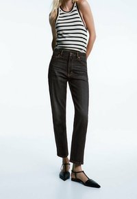 Jeans neri a vita alta con vestibilità a gamba dritta, abbinati a un top senza maniche a righe e décolleté nere con punta appuntita e cinturini alla caviglia.