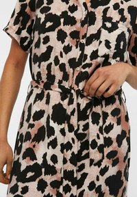 Kortärmad klänning i leopardmönster med nyanser av svart och mjuk rosa. Har skjortkrage, knappar och midjebälte.