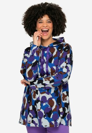 Tunic colorata con cappuccio che presenta un audace motivo di volti astratti in blu, marrone e nero. Realizzata in morbido tessuto con cordino.