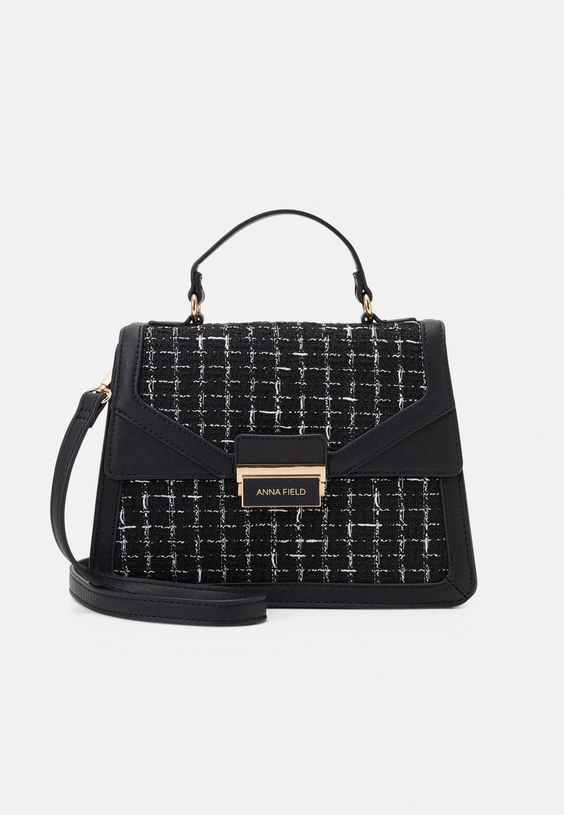 Mustavalkoinen tweedkäsilaukku tekonahkaisilla yksityiskohdilla, tasainen kahva, säädettävä hihna ja kullanvärinen lukon koriste edessä.