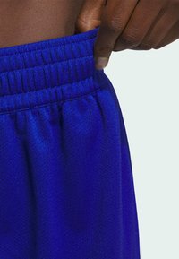 Blaue Sportshorts aus einem strukturierten, atmungsaktiven Mesh-Material mit einem elastischen Bund, der von einer Hand gehalten wird.