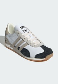 Sneaker bianca e grigia realizzata in pelle e suede, con tre strisce decorative, un logo nero sulla linguetta e suola in gomma.
