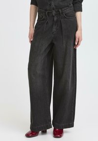 Pantaloni in denim neri a gamba larga con vita alta, caratterizzati da pieghe frontali e un classico design con cinque tasche. Il tessuto ha una texture morbida.
