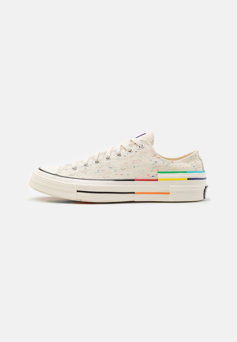 Sneakers z płótna o nakrapianej białej cholewce, z czarnymi i kolorowymi akcentami oraz niskim designem. Klasyczna gumowa podeszwa z osłoną palców.