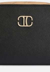 Portafoglio in pelle nera strutturata con logo metallico dorato intrecciato "TC" centrato vicino al bordo superiore.