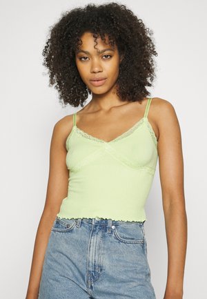 Top de alças verde-claro com nervuras e acabamento em renda, alças finas e bainha com babados. Combinado com calções de ganga de cintura alta.