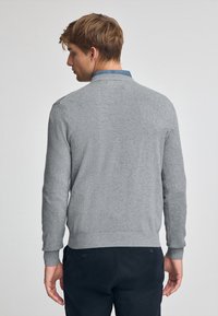 Grå stickad tröja med långa ärmar, ribbad nederkant och manschetter, med en enkel design och rund krage över en blå skjorta.