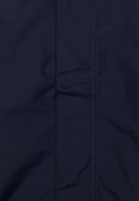Marineblauer Stoff mit glatter Textur, der eine zentrale Naht und subtile Falten aufweist, typisch für Softshell-Materialien, die in outerwear verwendet werden.