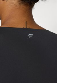 Schwarzes Sportoberteil mit glatter Textur und weitem Ausschnitt, mit einem kleinen weißen Logo auf der Rückseite in der Nähe des Kragens.