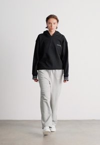 Mustapaitainen huppari logolla, yhdistettynä vaaleanharmaisiin collegehousuihin. Molemmat vaatteet ovat rentoa leikkuuta ja sileää kangasta, joissa on kontrastiväriset raidat.