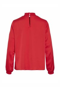 Blouse rouge à manches longues avec un col smocké. Le dos présente une ouverture en forme de clé et des poignets élastiqués. Tissu lisse et brillant.