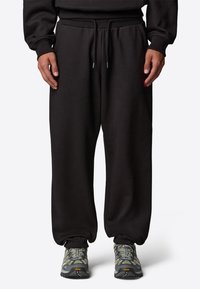 Czarne dresy z elastycznym pasem i sznurkiem, posiadające mankiety na końcach nogawek. Noszone z szaro-żółtymi, teksturowanymi butami sportowymi.