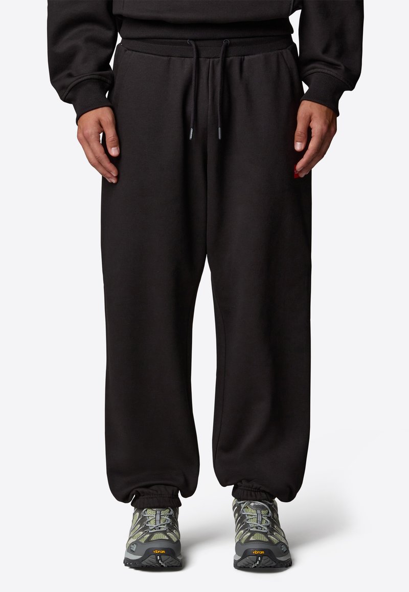 Czarne dresy z elastycznym pasem i sznurkiem, posiadające mankiety na końcach nogawek. Noszone z szaro-żółtymi, teksturowanymi butami sportowymi.