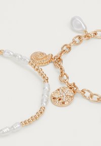Gold-tone bracelet featuring textured circular and spiral charms, interspersed with smooth white beads. Chain link design, elegant finish.