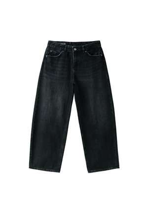 Personne portant un haut vert ample qu'elle soulève pour révéler le bas du dos, vêtue d'un jean noir taille haute avec des poches à l'arrière et une étiquette.