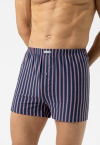 Herenboxers in marineblauwe stof met verticale rode en witte strepen. Heeft een elastische tailleband en een knoopsluiting aan de voorkant.