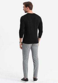 Schwarzes Langarmshirt, slim fit, kombiniert mit hellgrauen, maßgeschneiderten Hosen und schwarzen Turnschuhen. Glatte Textur, schlichtes Design, keine sichtbaren Muster.