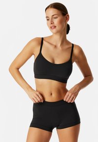 Sort træningsbh med tynde stropper og rund halsudskæring, parret med matchende højtaljede shorts. Glat stof, minimalistisk design.