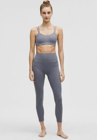 Sivi sportski grudnjak s tankim trakama uparen s visoko strukiranim, tijesnim sivim tajicama. Glatka tekstura i minimalistički dizajn.