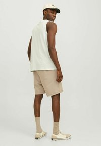 T-shirt sans manches gris clair, shorts beiges, casquette kaki, chaussettes beiges et baskets blanches. Accent mis sur un design simple et des couleurs neutres.