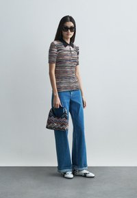 Πλεκτό πόλο μπλουζάκι με πολύχρωμη υφή, μαύρος γιακάς, συνδυασμένο με φαρδιά μπλε τζιν. Τα αξεσουάρ περιλαμβάνουν μια τσάντα με μοτίβο και παπούτσια χωρίς λουράκι.