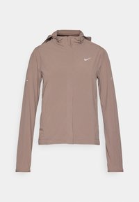 Chaqueta ligera en tono topo con capucha, mangas largas y cierre frontal. Presenta un pequeño logotipo blanco de Nike en el pecho y sutiles detalles en las mangas.