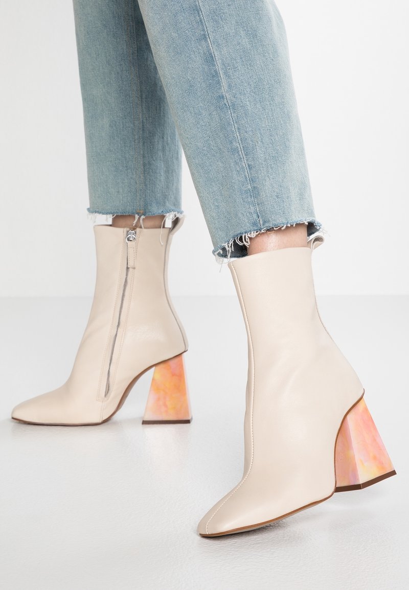 Bottes cheville beiges avec fermeture éclair, bouts pointus et talons larges multicolores marbrés, portées avec un jean bleu clair à bords effilochés.