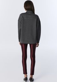 Maglione grigio con colletto alto e spalle scese, abbinato a leggings bordeaux lucidi. Tessuto morbido e design slim-fit.