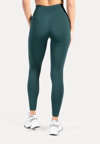 Hoog uitgesneden, teal kleurige leggings met een gladde textuur en een nauwsluitend ontwerp, gecombineerd met witte sneakers met zilveren accenten en logodetails.