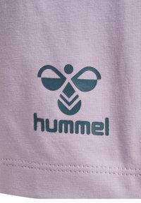 Lila stof heeft een donkerblauwe logo met een gestileerde bij en het woord "hummel" eronder. De textuur is soepel met een subtiel breipatroon.