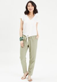 Haut à manches courtes blanc avec un détail à nouer à l'avant, associé à un pantalon vert clair et des sandales décoratives. Textures lisses, coupe décontractée.