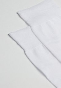 Chaussettes blanches en coton avec un tricot texturé, présentant une bordure supérieure lisse et un talon renforcé. Le matériau semble doux et flexible.