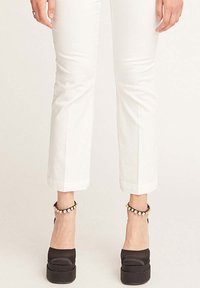 Scarpe platform nere con una superficie liscia, dotate di cinturini alla caviglia decorati con perle simili a perle. Pantaloni bianchi aderenti con una finitura pulita.